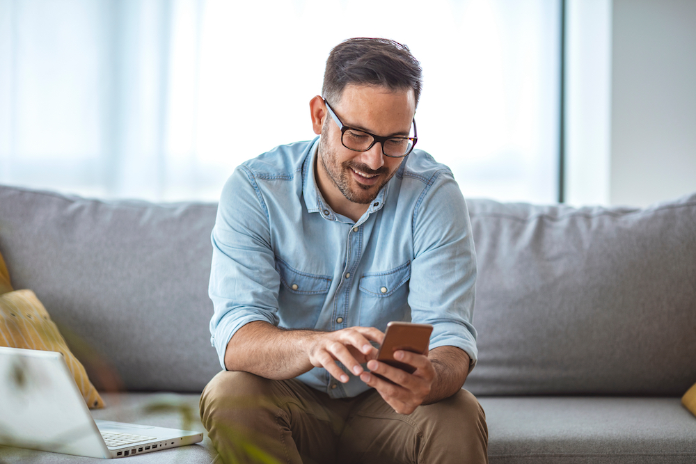 Man sitting on couch while looking at smartphone at home