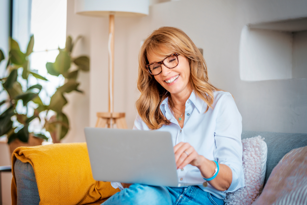Happy middle aged woman using her laptop on the sofa at home.